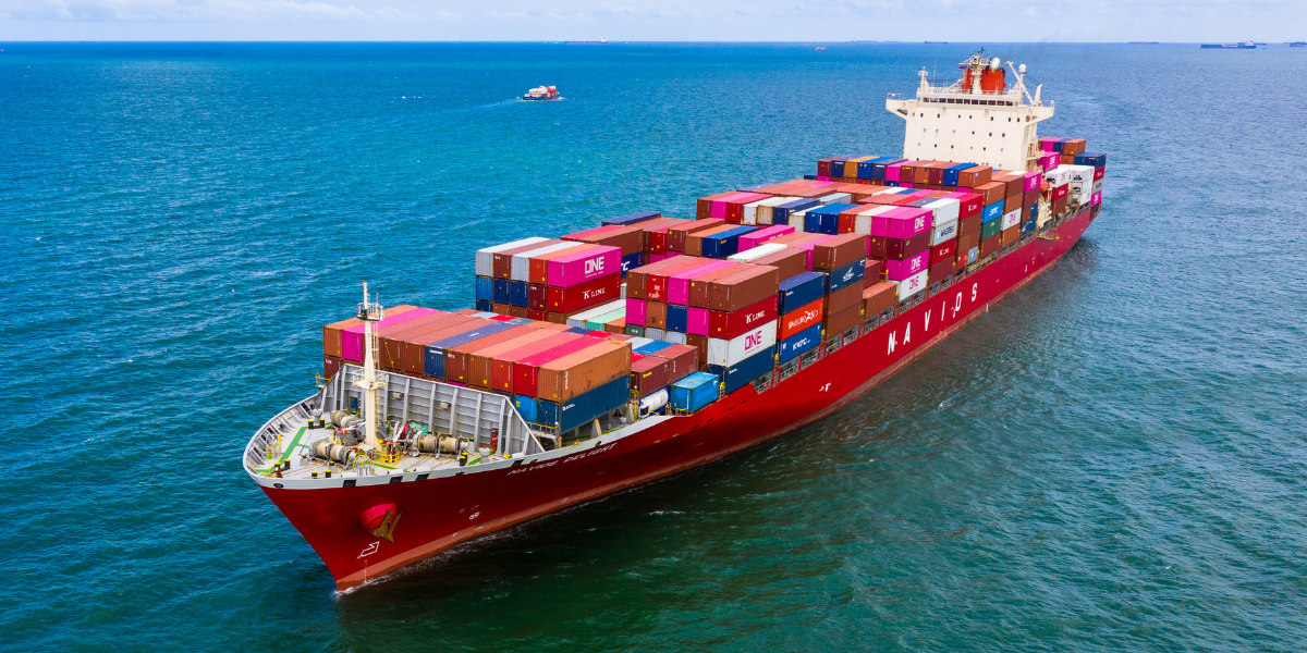 Red cargo ship carrying many storage containers across the ocean