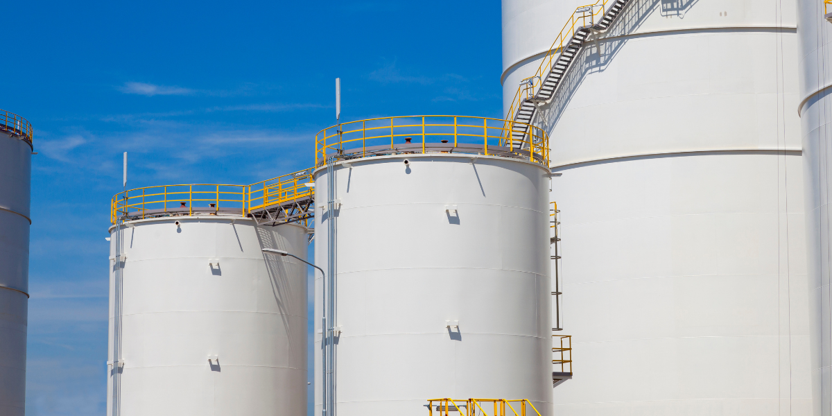 several large white tanks with yellow ladders in front of a blue sky